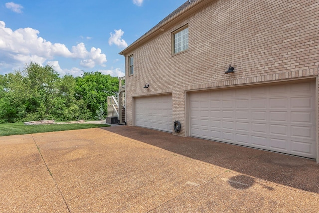 view of property exterior featuring a garage, central AC, brick siding, concrete driveway, and stairway