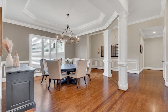 dining room featuring a tray ceiling, decorative columns, wood finished floors, and a chandelier