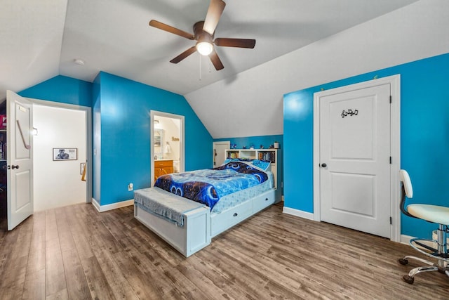 bedroom featuring wood finished floors, a ceiling fan, baseboards, ensuite bath, and lofted ceiling