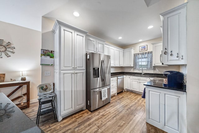 kitchen featuring white cabinets, appliances with stainless steel finishes, light wood-style flooring, and a sink