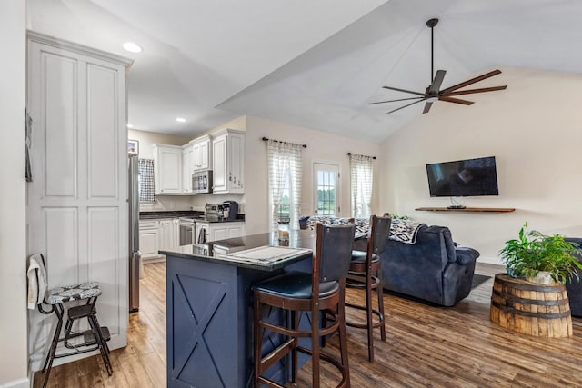 kitchen with wood finished floors, a ceiling fan, dark countertops, appliances with stainless steel finishes, and recessed lighting