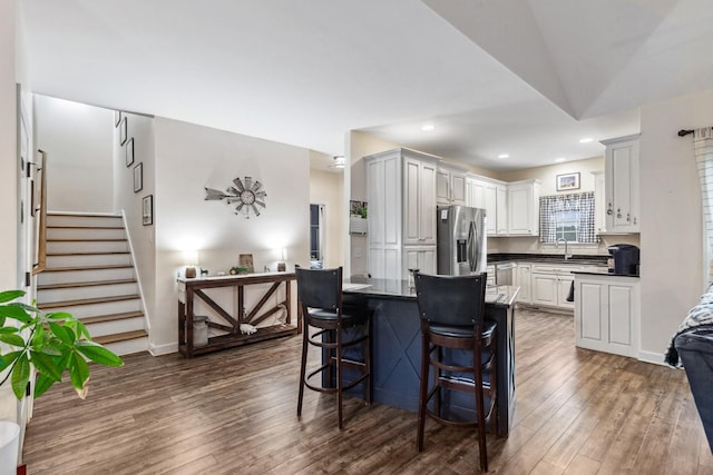 kitchen with stainless steel fridge with ice dispenser, dark countertops, dark wood finished floors, and a kitchen breakfast bar