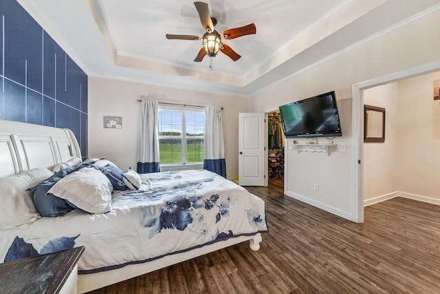 bedroom featuring baseboards, crown molding, a walk in closet, a raised ceiling, and wood finished floors