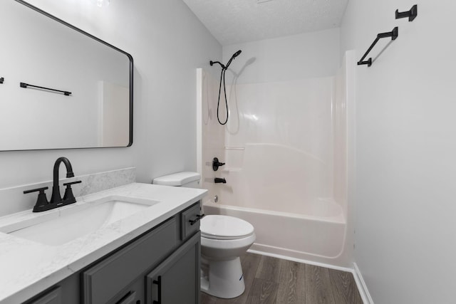 bathroom featuring a textured ceiling, wood finished floors, shower / washtub combination, vanity, and toilet