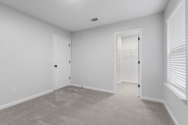 unfurnished bedroom featuring a walk in closet, carpet, baseboards, visible vents, and a closet