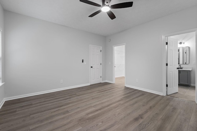 unfurnished bedroom featuring ceiling fan, a sink, ensuite bath, baseboards, and wood finished floors