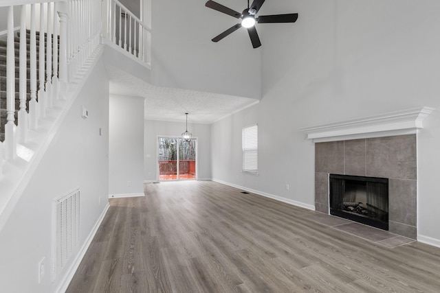 unfurnished living room with a high ceiling, a ceiling fan, wood finished floors, a tile fireplace, and visible vents
