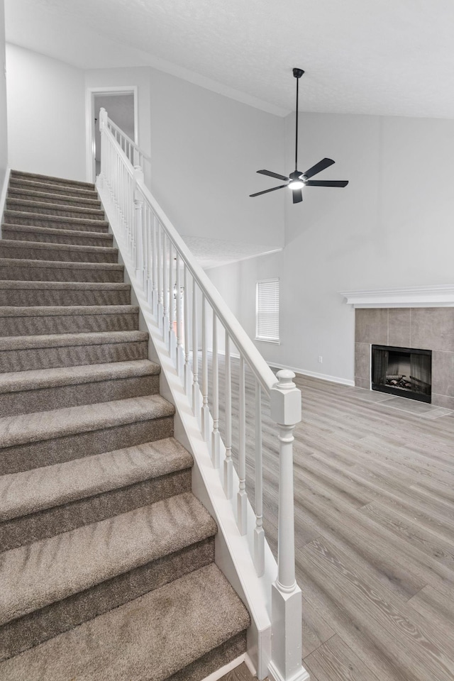 stairs featuring a ceiling fan, baseboards, wood finished floors, and a fireplace