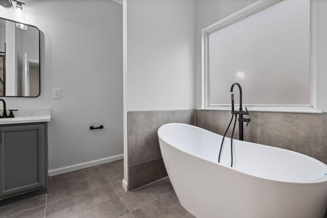 bathroom with a freestanding tub, vanity, tile patterned flooring, and tile walls
