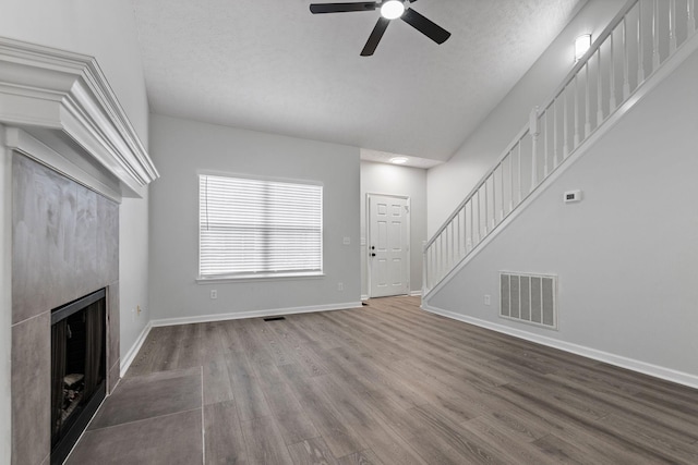 unfurnished living room with visible vents, stairs, wood finished floors, a fireplace, and a ceiling fan