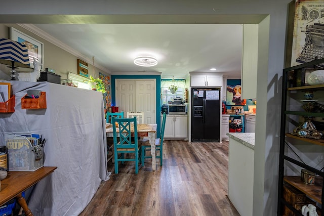 interior space with black fridge with ice dispenser, crown molding, wood finished floors, stainless steel microwave, and white cabinets