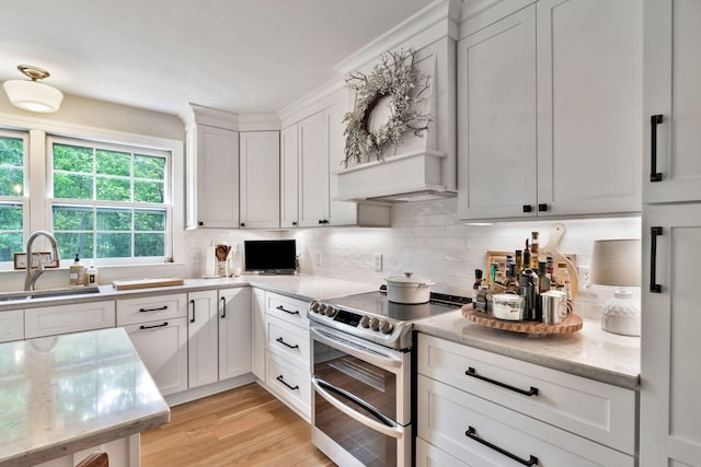 kitchen featuring a sink, range with two ovens, light wood-type flooring, white cabinetry, and decorative backsplash