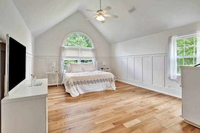 bedroom with light wood-style floors, a decorative wall, a wainscoted wall, and multiple windows