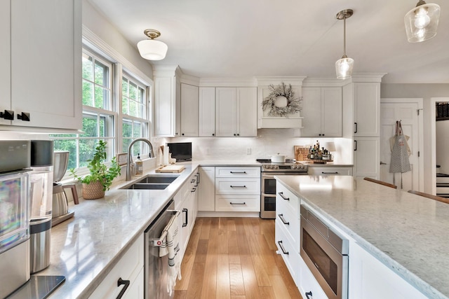 kitchen featuring a sink, light stone counters, white cabinets, hanging light fixtures, and appliances with stainless steel finishes