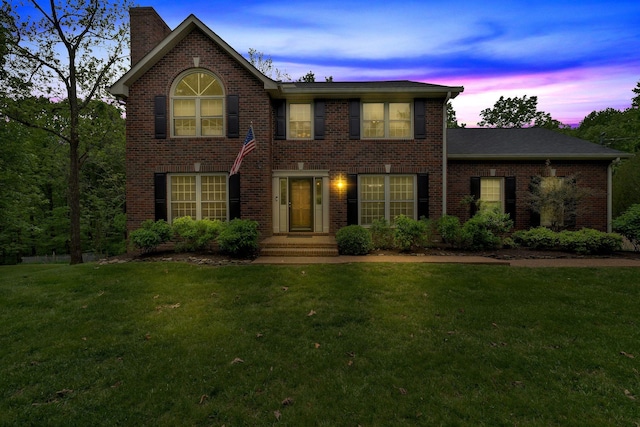 colonial-style house with a front lawn, a chimney, and brick siding