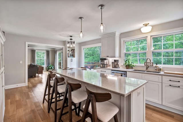 kitchen with a sink, dishwasher, a kitchen island, and white cabinets