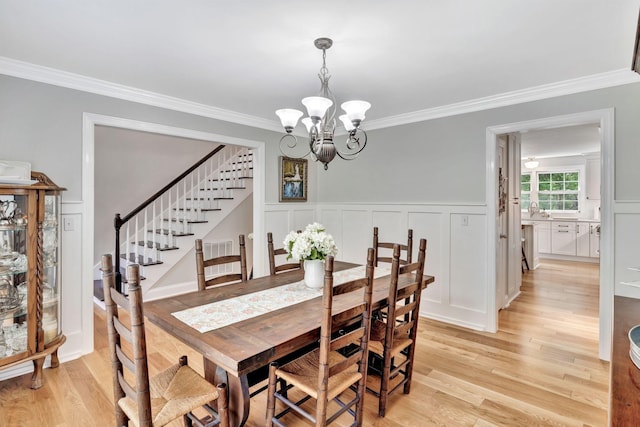 dining room with light wood finished floors, crown molding, stairway, and an inviting chandelier