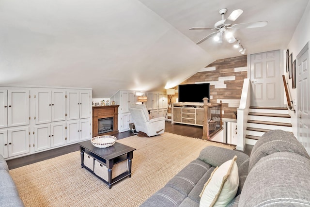 living area featuring a ceiling fan, dark wood-style flooring, a glass covered fireplace, and vaulted ceiling