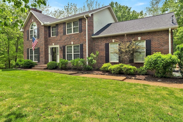 colonial home featuring a shingled roof, brick siding, and a front yard