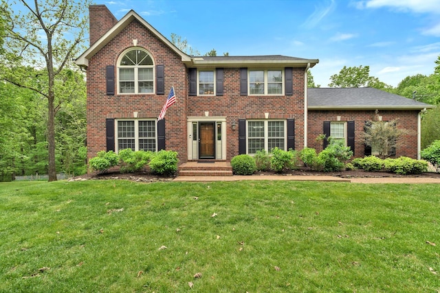 colonial inspired home featuring brick siding, a chimney, and a front yard