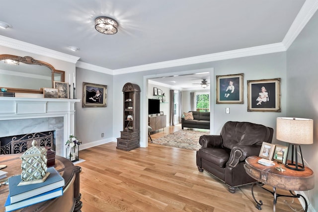 living area featuring baseboards, ornamental molding, light wood finished floors, ceiling fan, and a high end fireplace