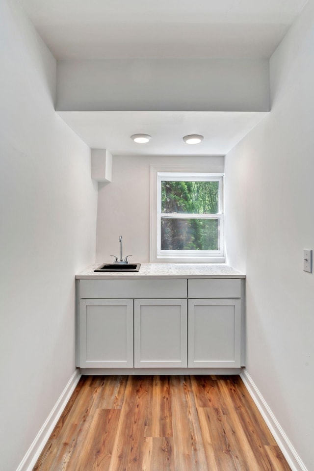 bar with light wood finished floors, baseboards, and a sink