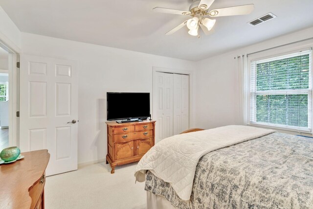 bedroom featuring a closet, baseboards, ceiling fan, visible vents, and light colored carpet