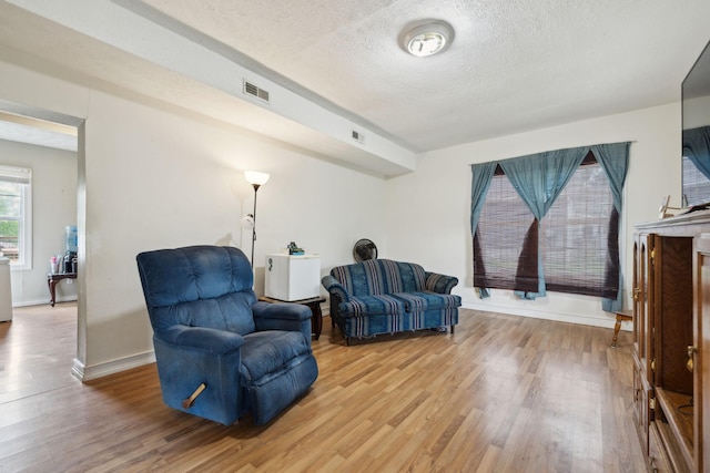 living area with visible vents, a textured ceiling, light wood finished floors, and baseboards