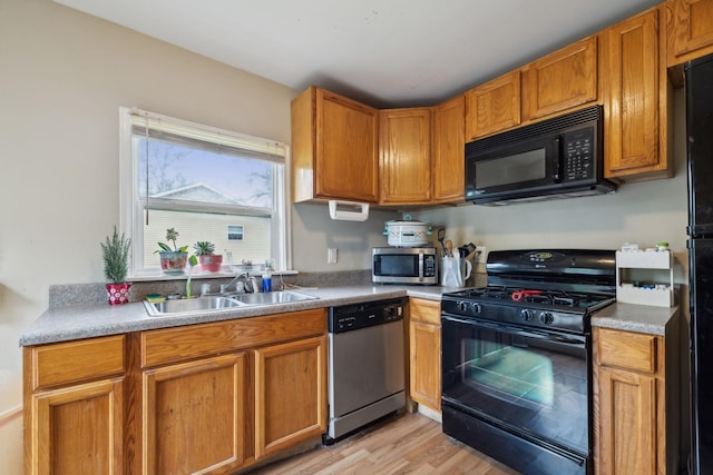 kitchen with a sink, brown cabinets, black appliances, and light wood finished floors