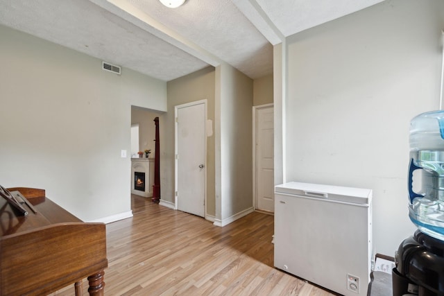 interior space featuring a lit fireplace, baseboards, visible vents, and light wood-type flooring