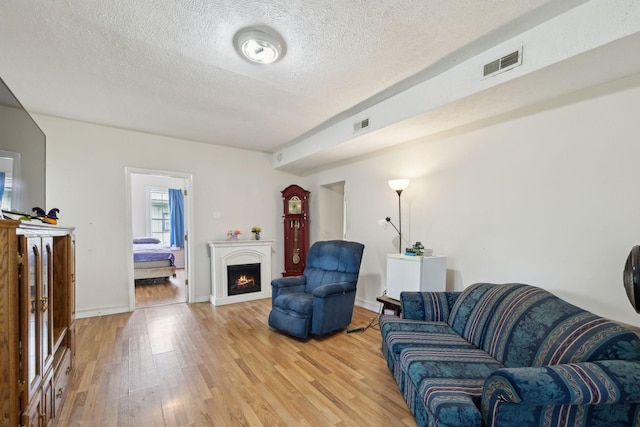 living room featuring a lit fireplace, a textured ceiling, visible vents, and light wood finished floors