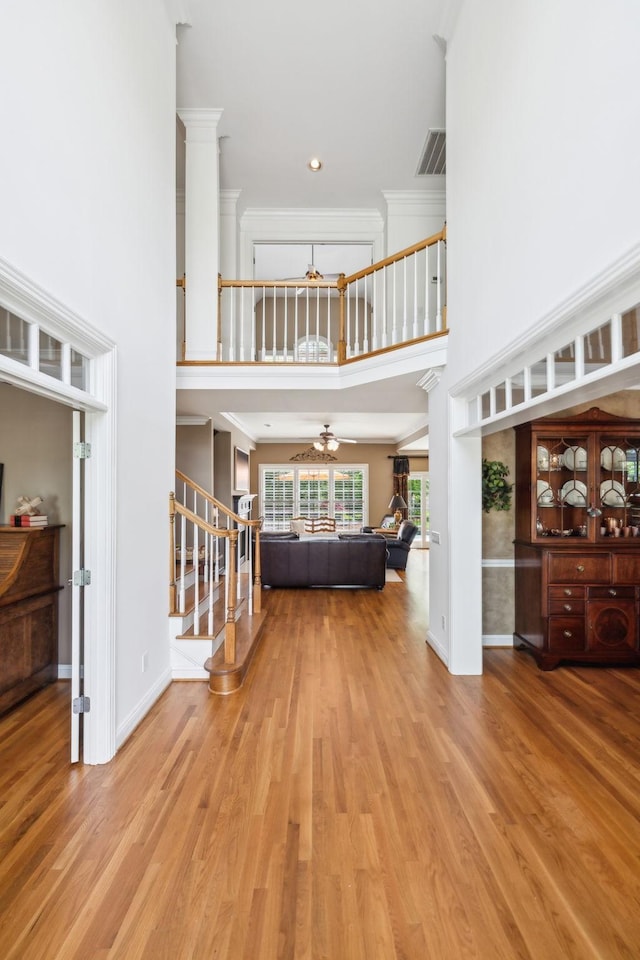 foyer entrance featuring crown molding, stairway, baseboards, light wood finished floors, and a high ceiling