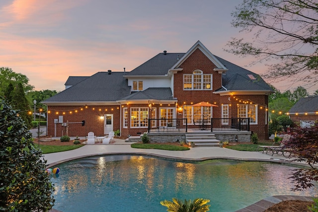 back of house at dusk with brick siding, a wooden deck, an outdoor pool, and a patio area