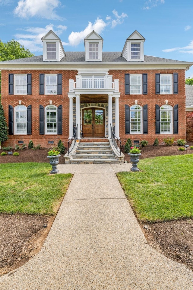 view of front of home with brick siding, a balcony, and a front yard
