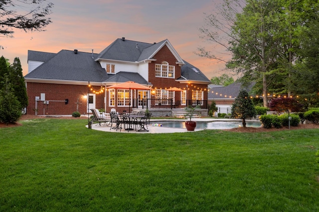 back of house at dusk featuring a lawn, a patio area, an outdoor pool, and brick siding