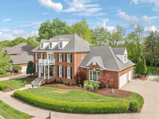 georgian-style home featuring driveway, brick siding, fence, a balcony, and a front lawn
