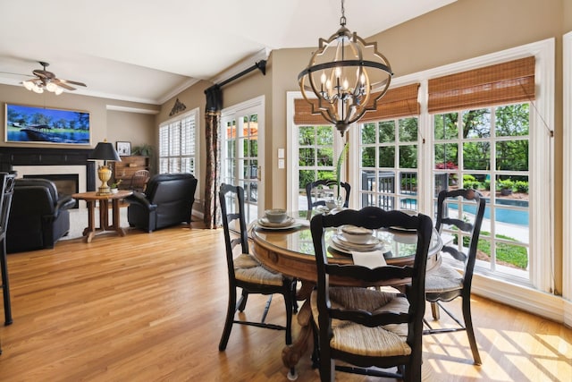 dining room featuring crown molding, light wood-style flooring, ceiling fan with notable chandelier, and a fireplace