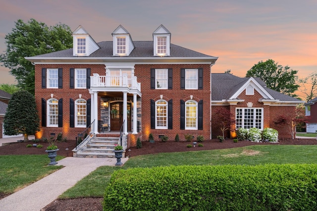 colonial-style house featuring a front yard, brick siding, and a balcony