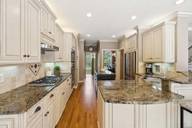 kitchen featuring backsplash, a peninsula, appliances with stainless steel finishes, and a sink
