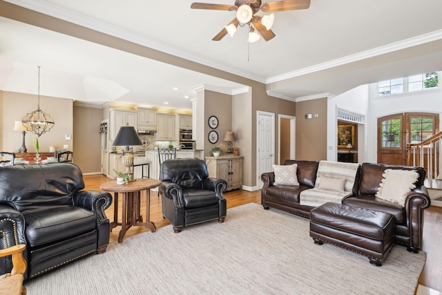 living area with baseboards, ornamental molding, ceiling fan with notable chandelier, and light wood-type flooring