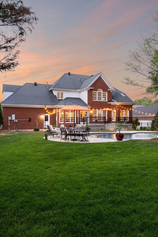 rear view of property with a patio, a yard, an outdoor pool, and brick siding
