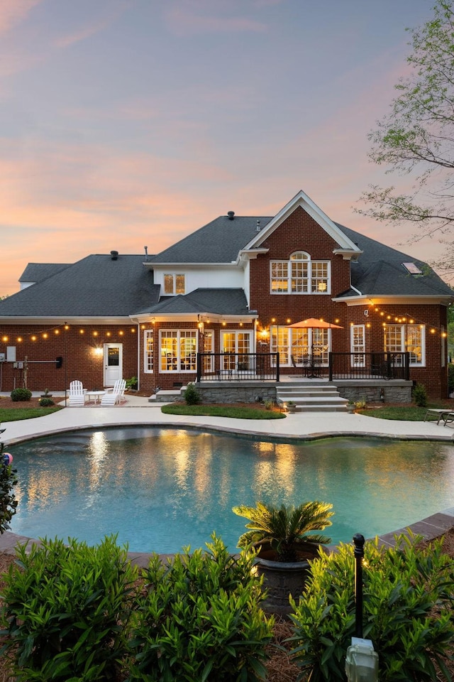 pool at dusk featuring french doors, a wooden deck, and an outdoor pool
