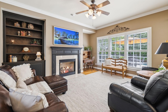 living room featuring light wood-style flooring, a ceiling fan, baseboards, a high end fireplace, and ornamental molding