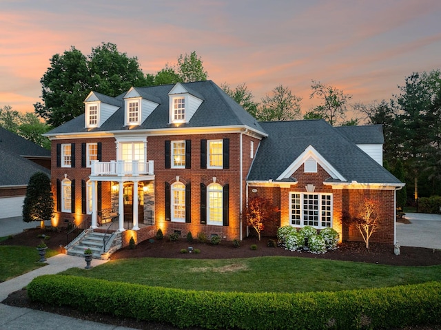 colonial inspired home featuring brick siding, a balcony, a front yard, and covered porch