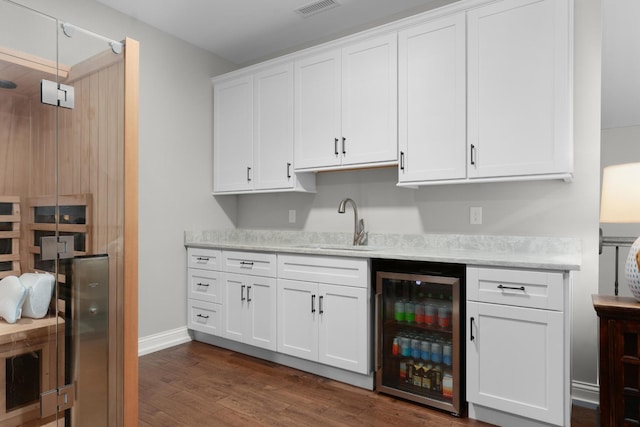 bar featuring visible vents, a sink, baseboards, beverage cooler, and dark wood-type flooring
