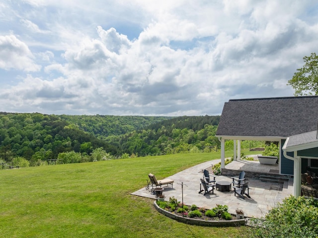 view of yard featuring a patio, a fire pit, and a wooded view