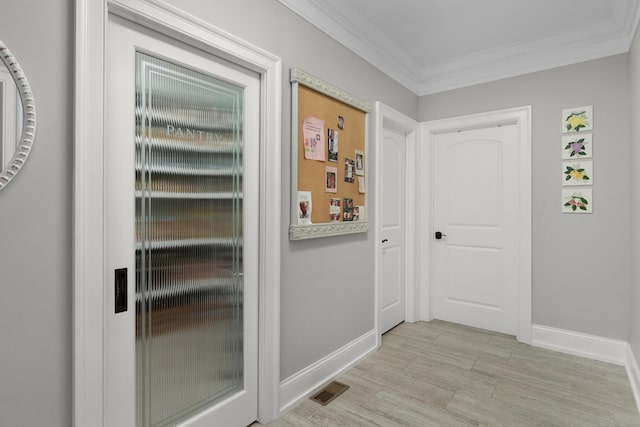 doorway with crown molding, baseboards, visible vents, and light wood finished floors