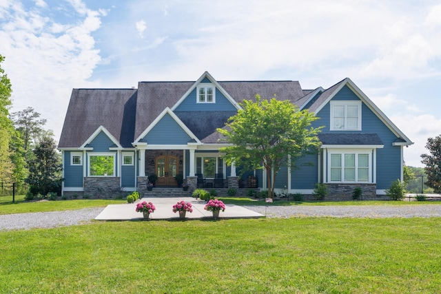 craftsman-style house with a porch, roof with shingles, a front yard, and stone siding