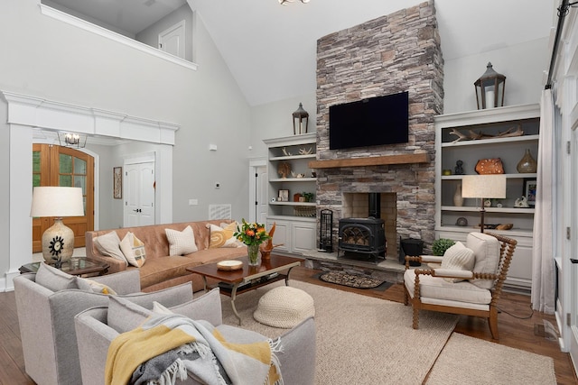 living area with high vaulted ceiling, a chandelier, wood finished floors, and a wood stove