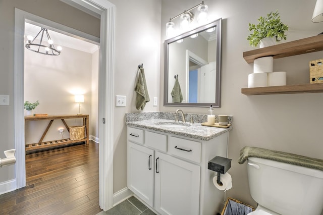 bathroom with toilet, wood finished floors, baseboards, a chandelier, and vanity